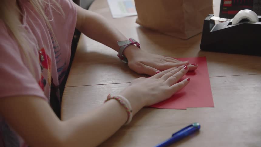 Girl sitting on table folds paper to make a card