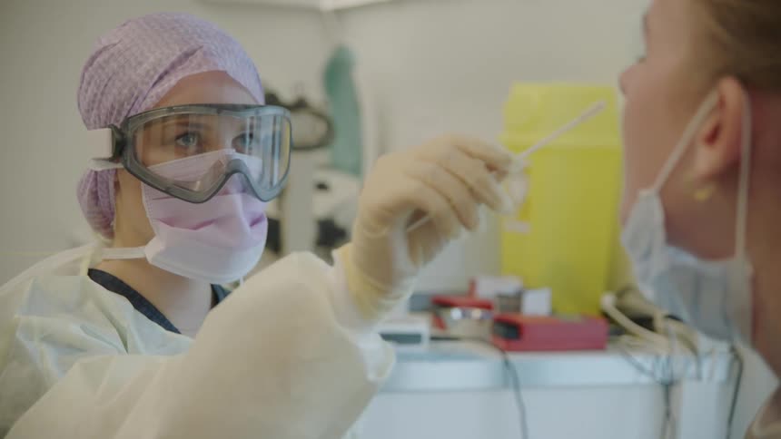A medical professional in protective gear swabbing the nose of a female patient