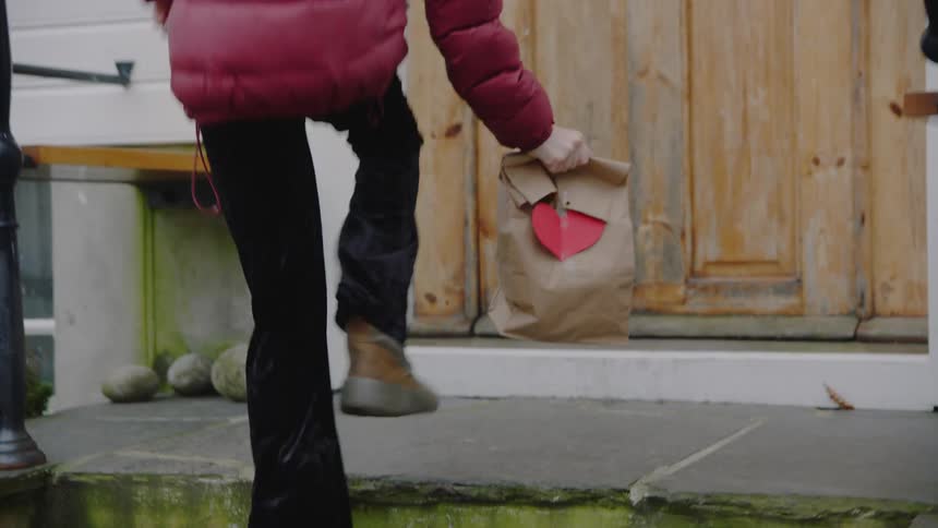 Young girl running to doorstep and dropping of a paper bag with a heart on it