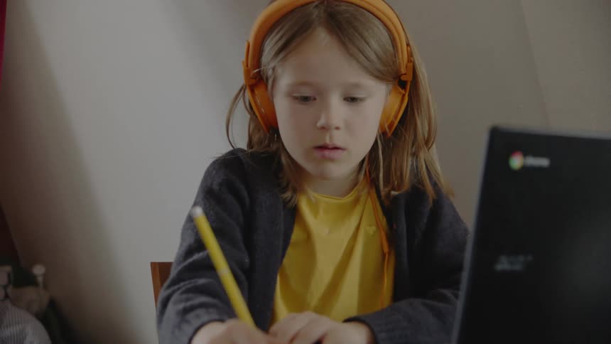 A girl with headphones a pencil and paper and a laptop