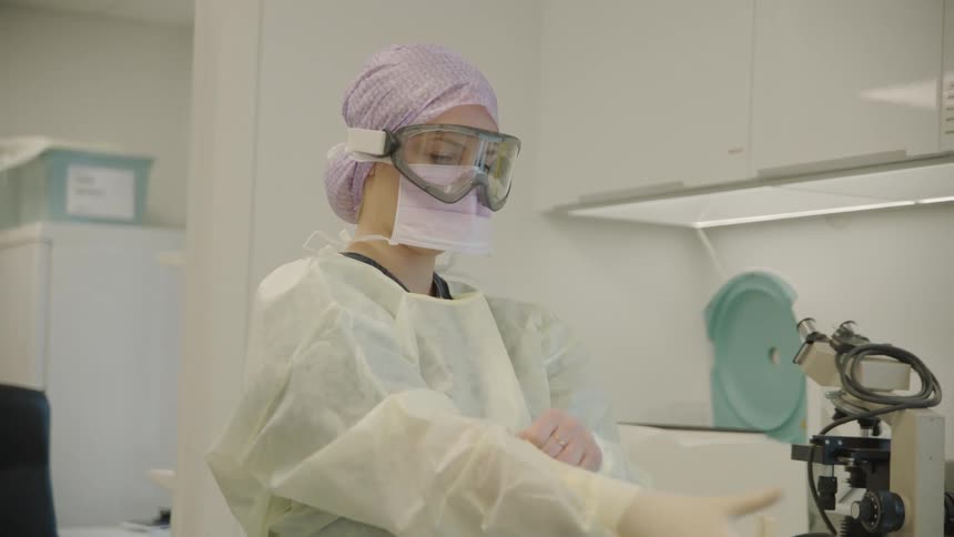 A white woman in medical protective gear puts on a rubber glove