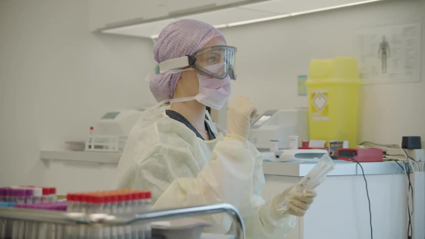 A woman wearing ppe in a lab grabs packaged equipment