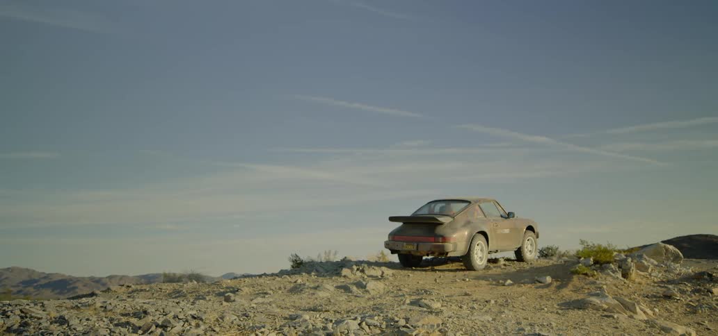 A dust and dirt covered sports car is parted on a rocky dirt ridge outdoors