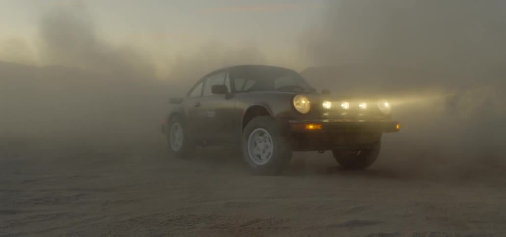 A car sits in the sand with dust all around it and then drives off