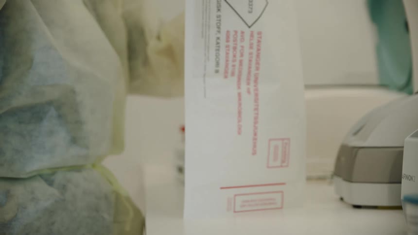 A woman with disposable gloves and a mask putting tubes in a envelope