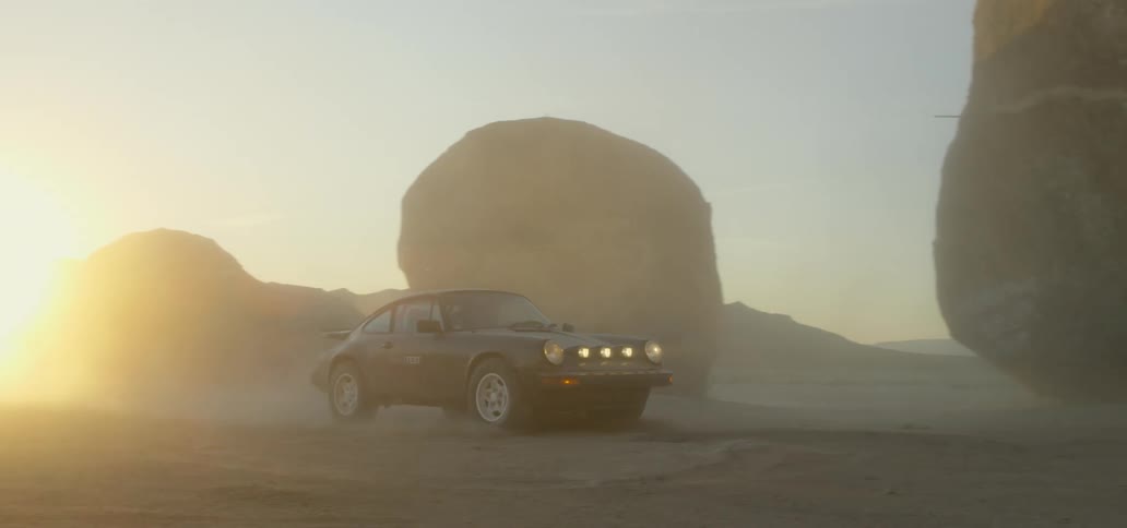 Car with headlights on drives through boulders at sunset
