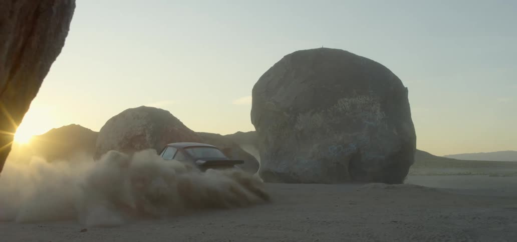 A sports car throwing up a cloud of dust as it drifts around a set of boulders
