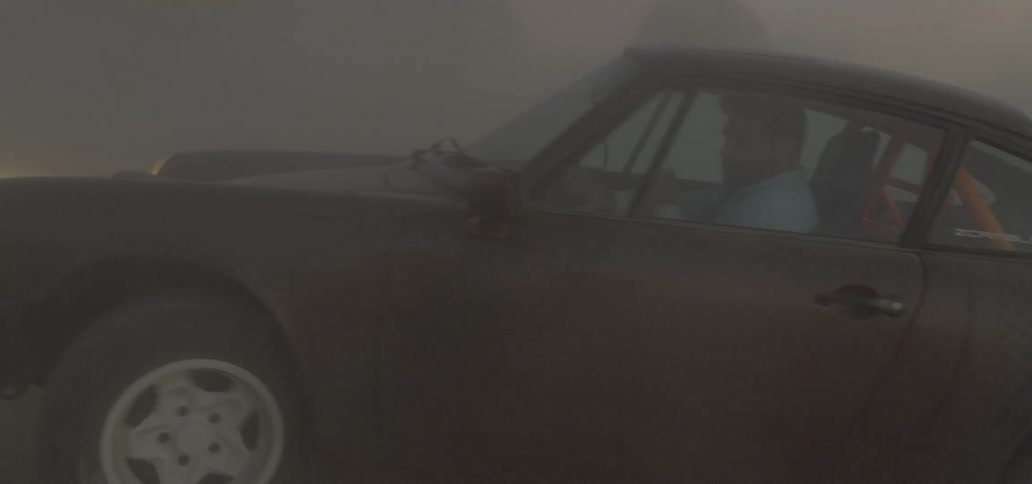 Sports car with headlights on driving on the sands of desert at sunset