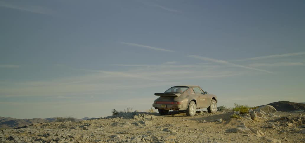 A dusty car sits on a rocky section of land