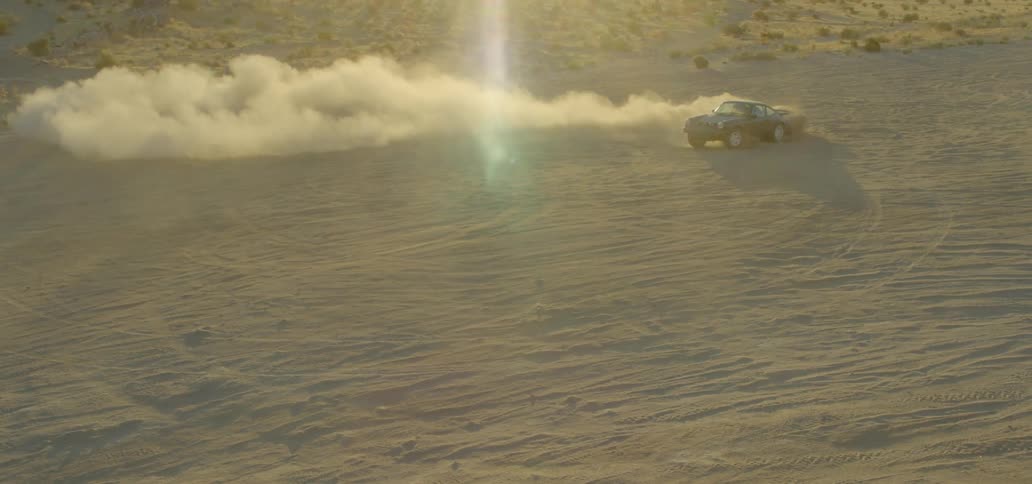 A sports car does donuts in the sand kicking up a circle of dust