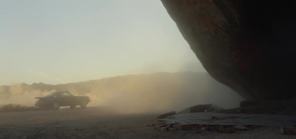 Car kicks up dust as it spins near a cliff wall