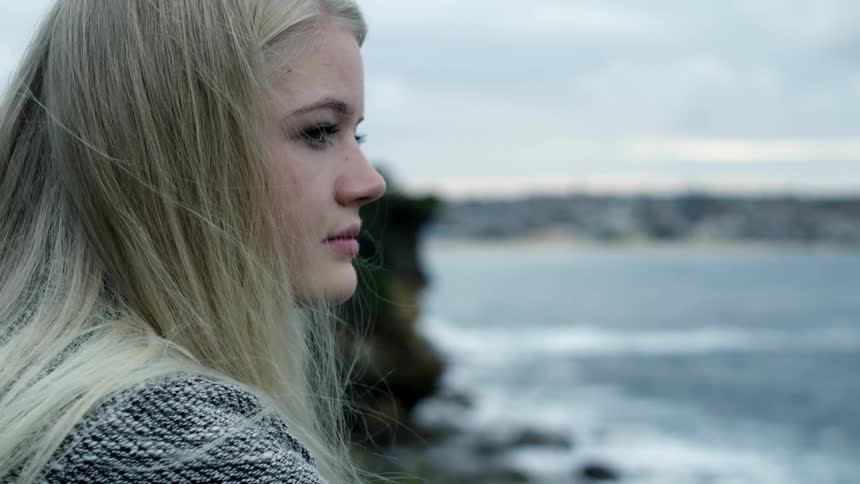 A woman is looking around by the shore on a cloudy day