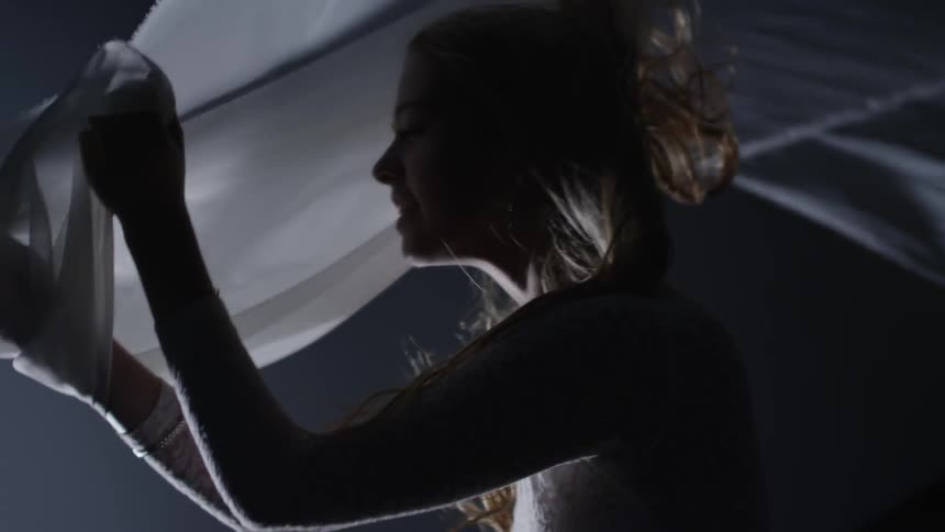 A woman holding a white scarf as it billows in the wind and her hair blows around her face