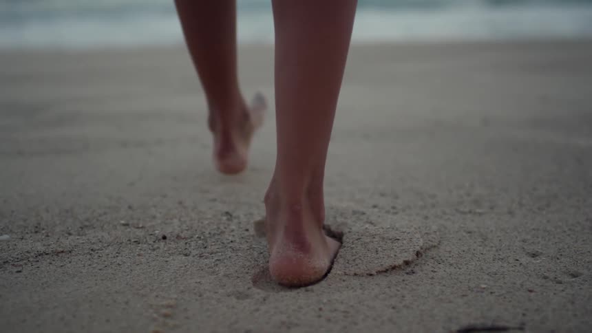 Close up of someone's feet as they walk through sand and leave deep footprints