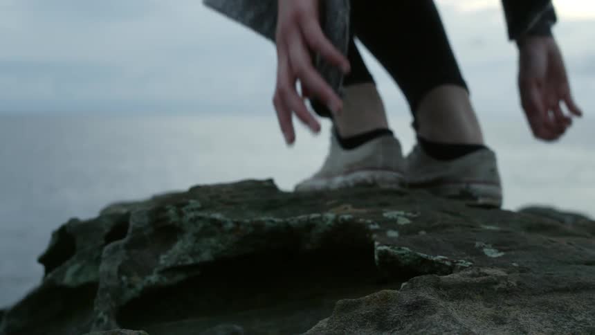 A woman walks to the edge of a rock and sits down