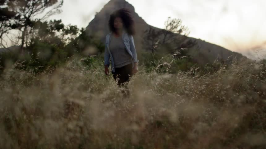 A woman walks slowly through tall dry grass