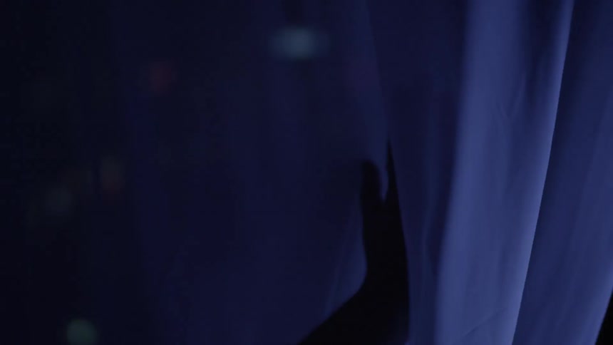 A woman touches a filmy curtain in the dark