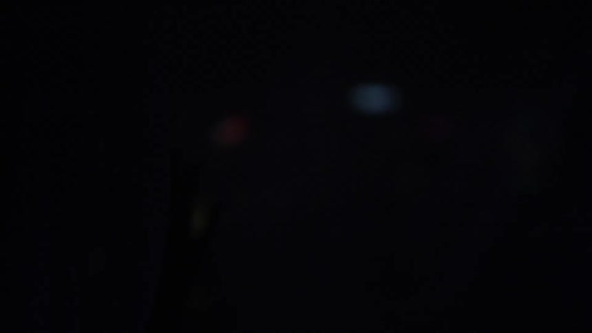 A woman wearing rings and pearl bracelets caressing sheer curtains as lights pulse on and off