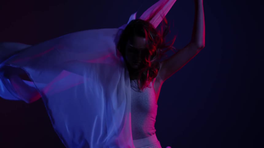 A woman is twirling around a scarf in a dark area