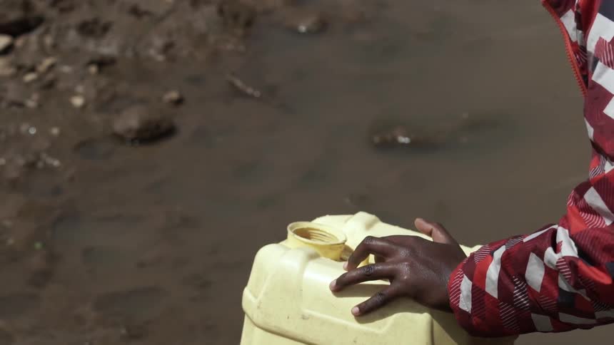 Hands are seen using a large mug to draw water from a dirty stream and pour it into a container