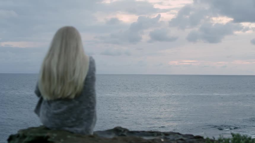 A woman sits overlooking the ocean on a cloudy day