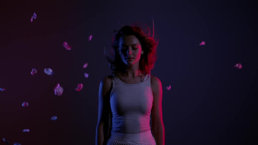 A woman is standing in a dark area as flower petals fly around