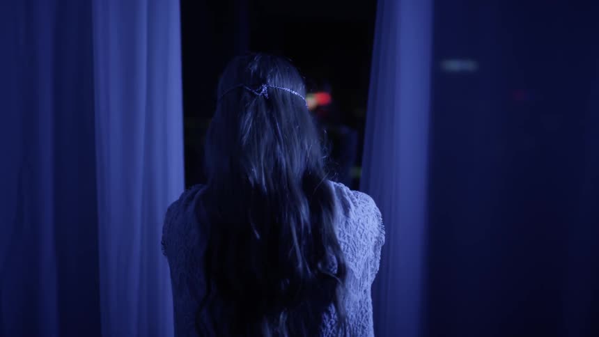 A woman stands at a window at night