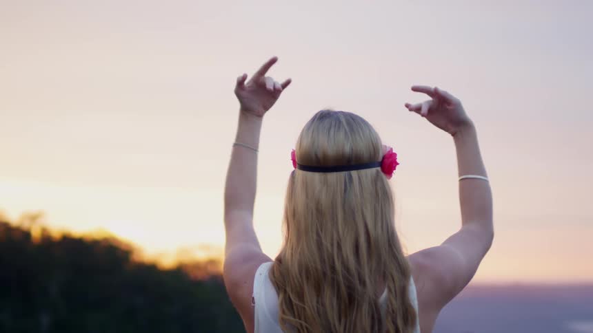 A woman waves her arms around outside at sunset