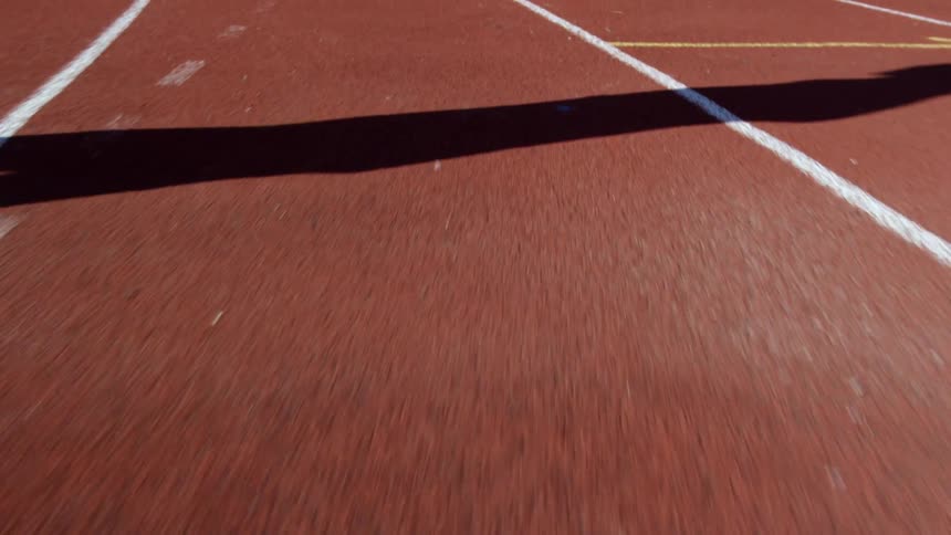 A runner's shadow is cast on a racing track