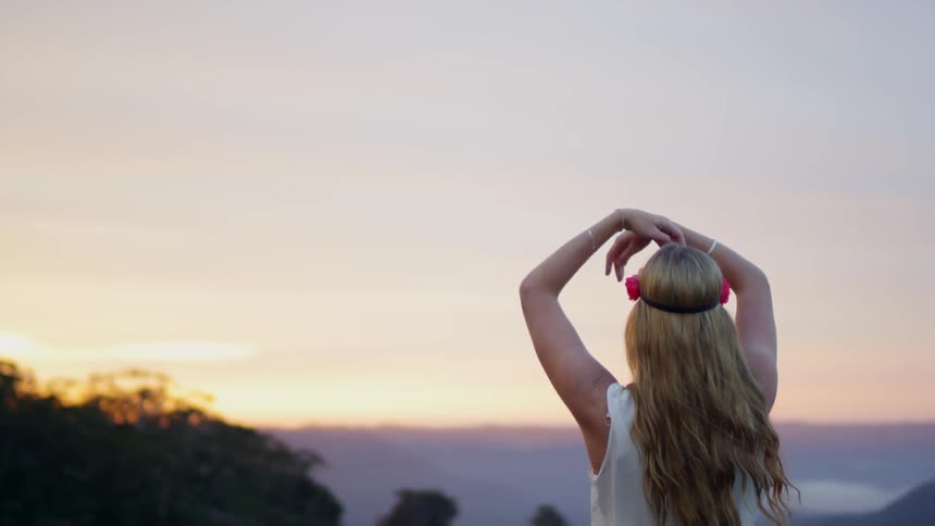 A woman waves her arms around outside at sunset