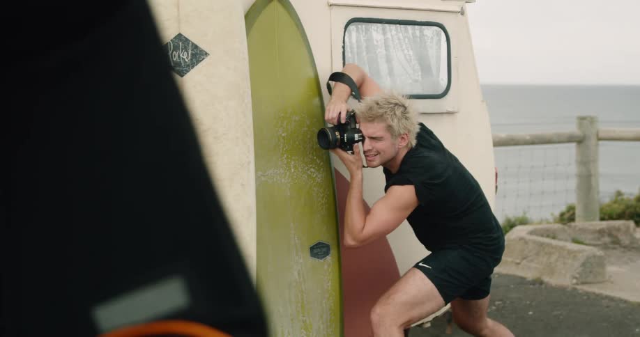 A blonde white man stands next to a trailer and takes photographs with a camera