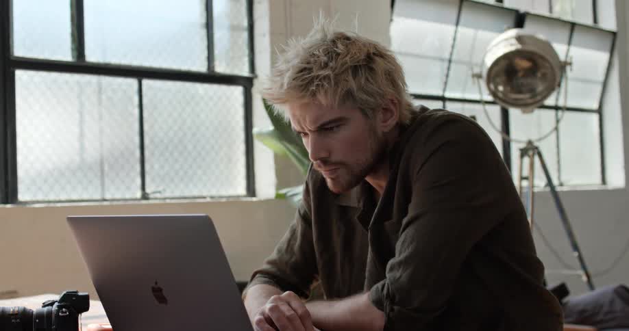 Man sits at table reading on laptop computer near windows