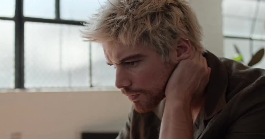 A man sitting at a desk leans on one arm while using the trackpad of a laptop