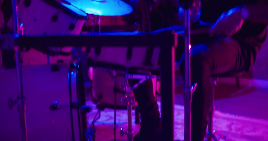 Drummer plays in room lit with purple light