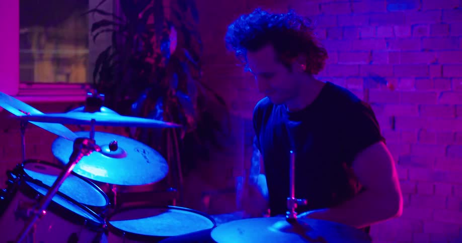 A bluish light shines on a man playing the drums at night