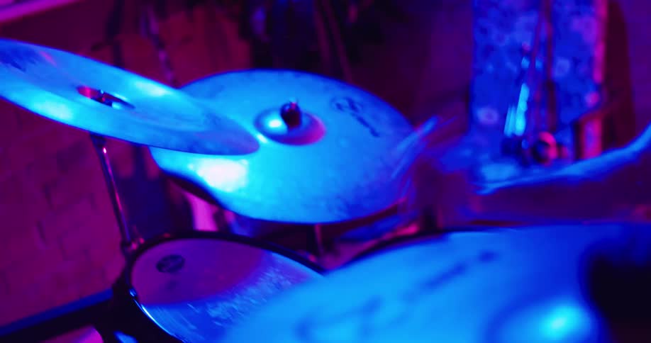 A man uses drum sticks to hit a drum set in a dimly lit space