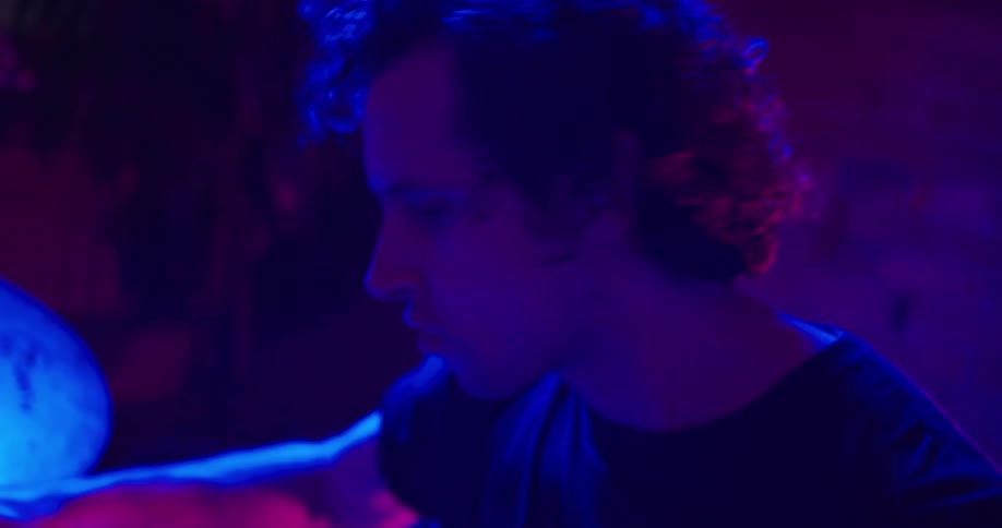 A male drummer performs at his drum set while lit by a blue light