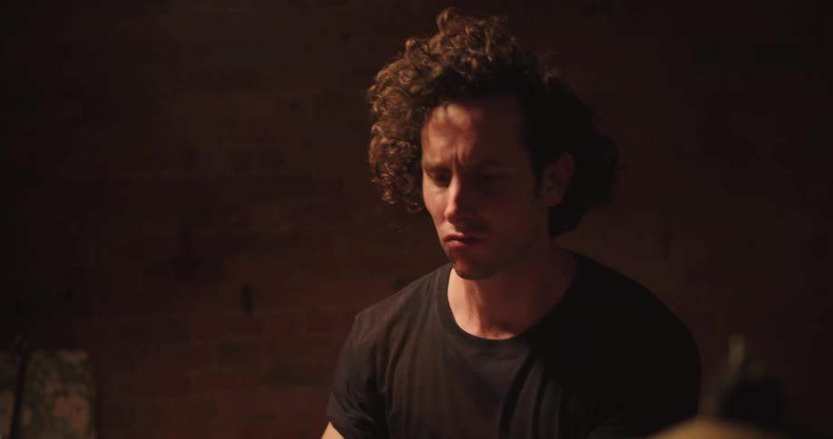 A man with curly hair plays drums