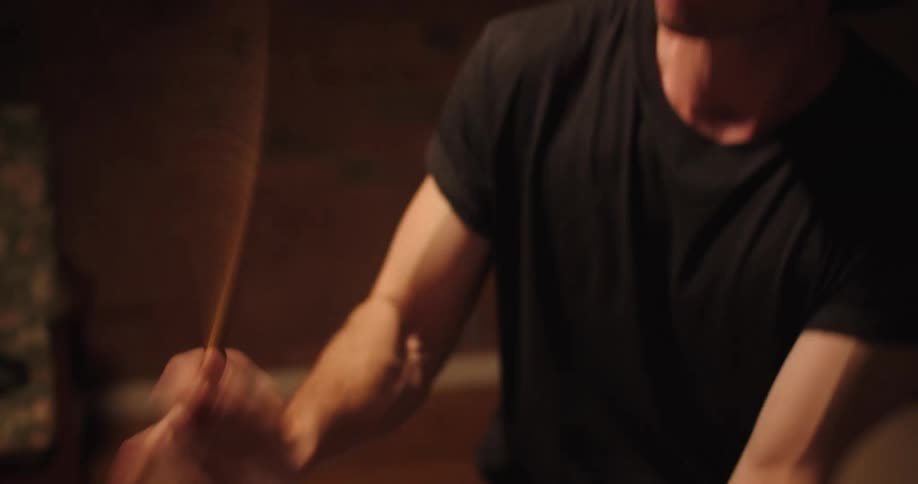A young male with curly hair speedily strikes a set of drums with his drum sticks