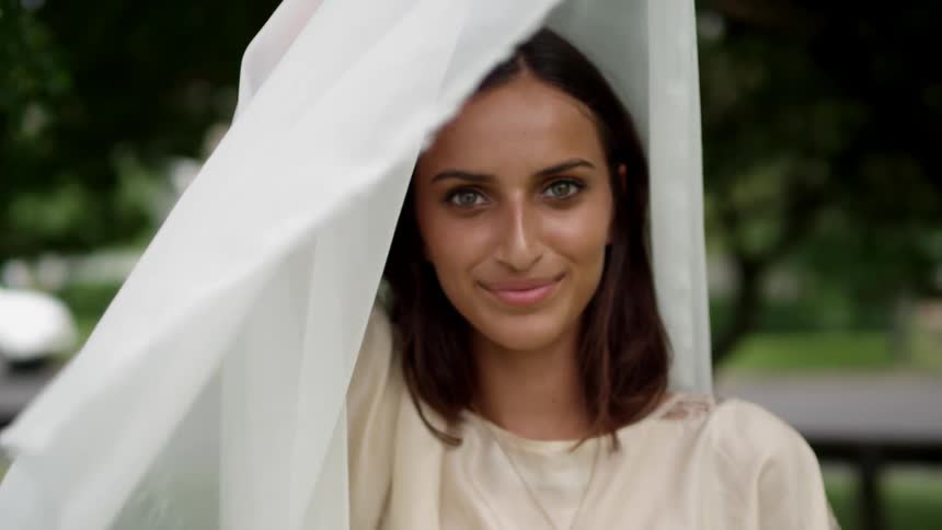 White fabric billows around a woman's face on a summer day