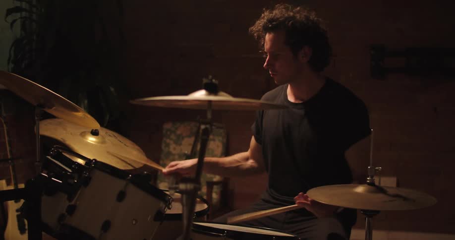 A man plays the drums in a darkened room