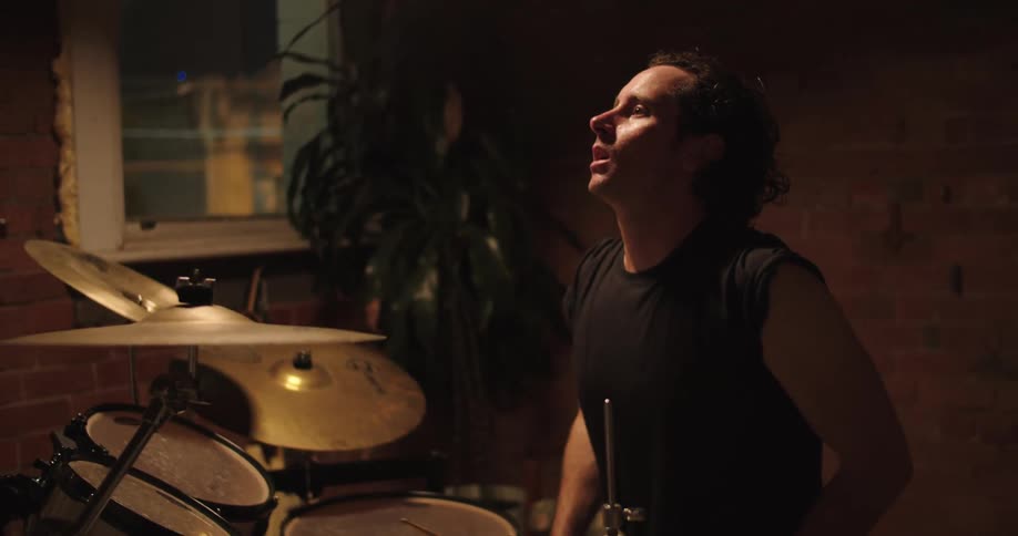 A man practices drumming in a dark room and stops to take a breath