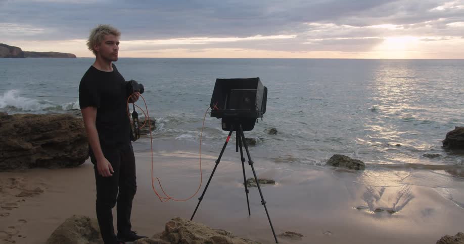 A blonde white man prepares to take pictures on a beach