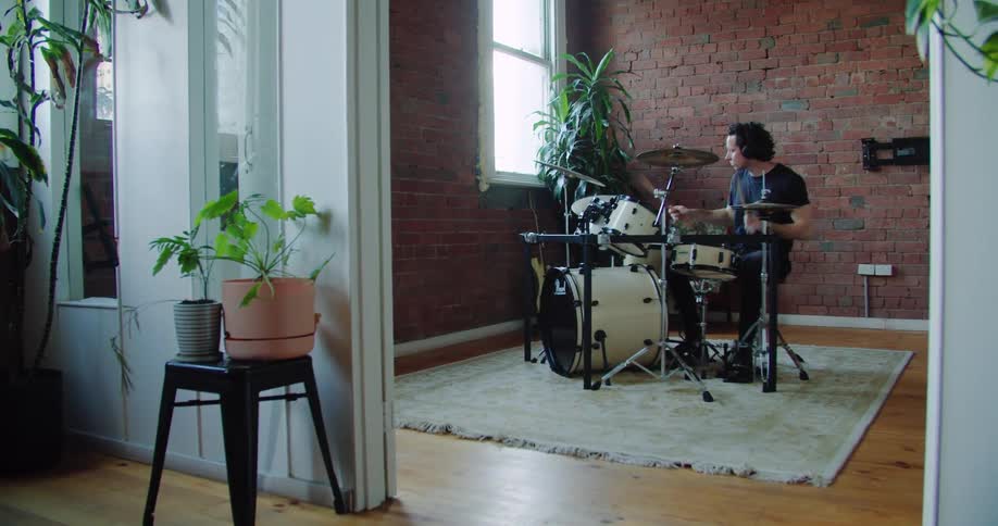 Man plays drums near window in room with brick wall