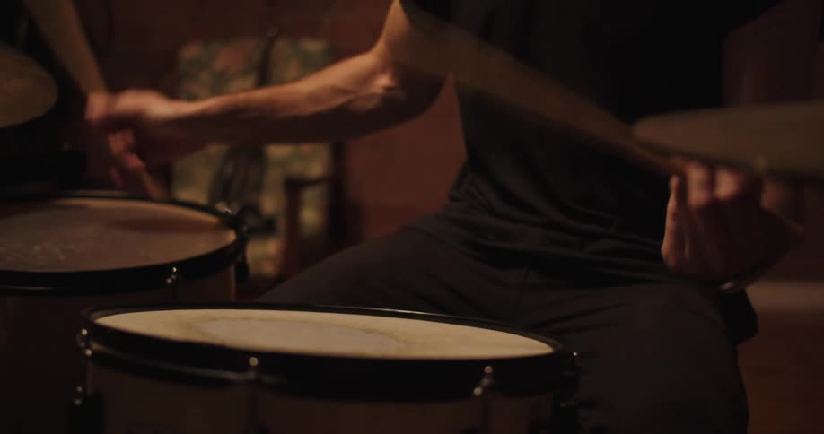 A mans arms and muscles strain as he plays the drums