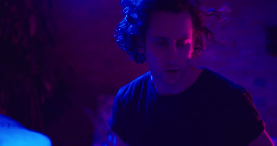 A man drums in a dark room with blue and pink lights