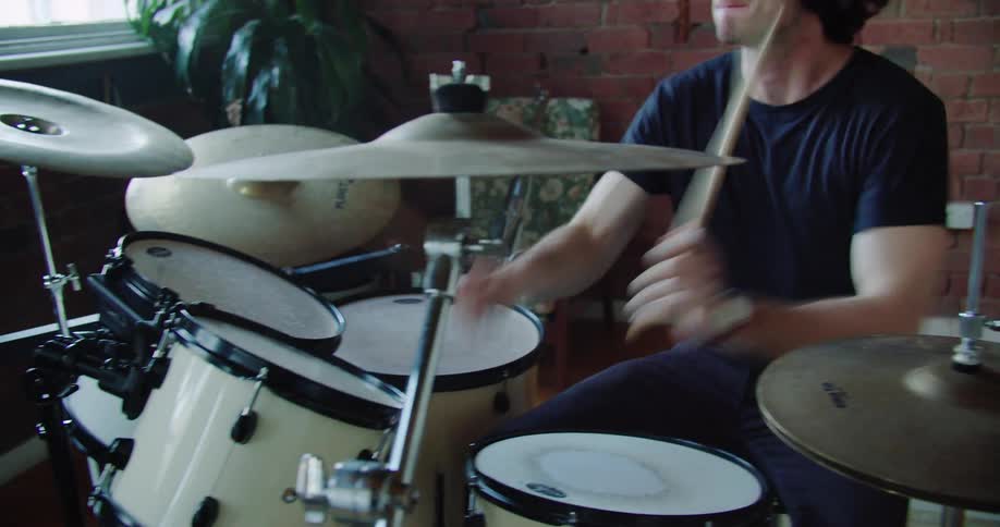 A male drummer quickly strikes his drums and cymbals with drum sticks