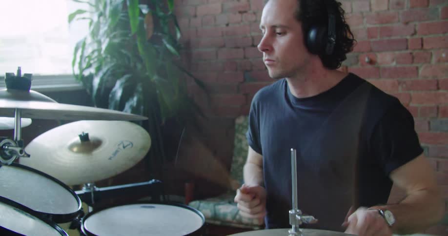 A male drummer wearing headphones plays the drums with a lot of energy