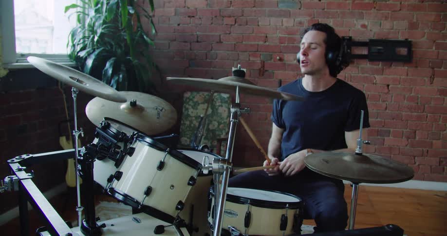 A man plays the drums and adjusts his headphones
