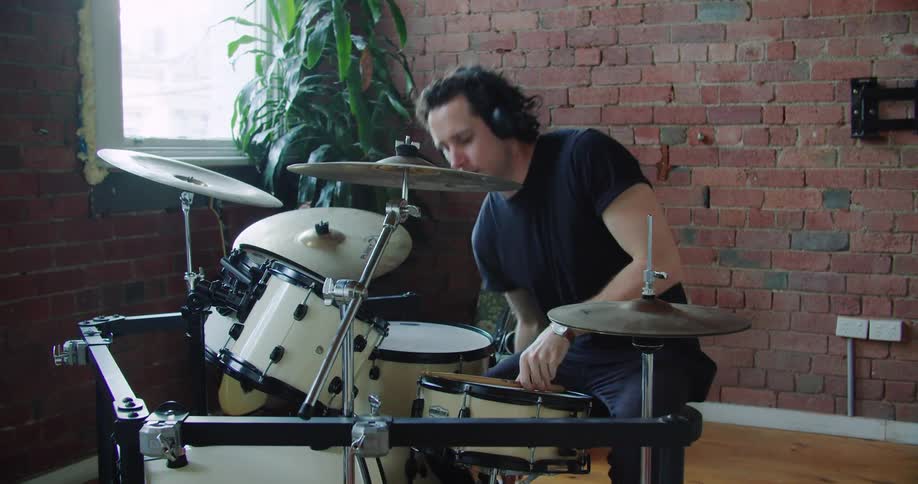 A man puts down his phone adjusts his headphones and stretches before playing the drums
